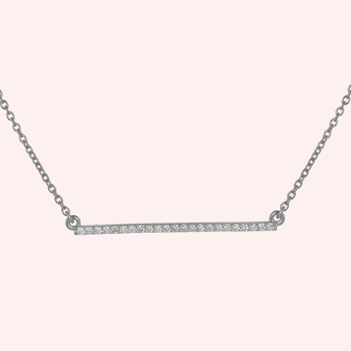 Gemstone_necklace_in_sterling_silver_in_a_bar_design_with_CZ_stones_at_front_angle_view_on_solid_pink_background