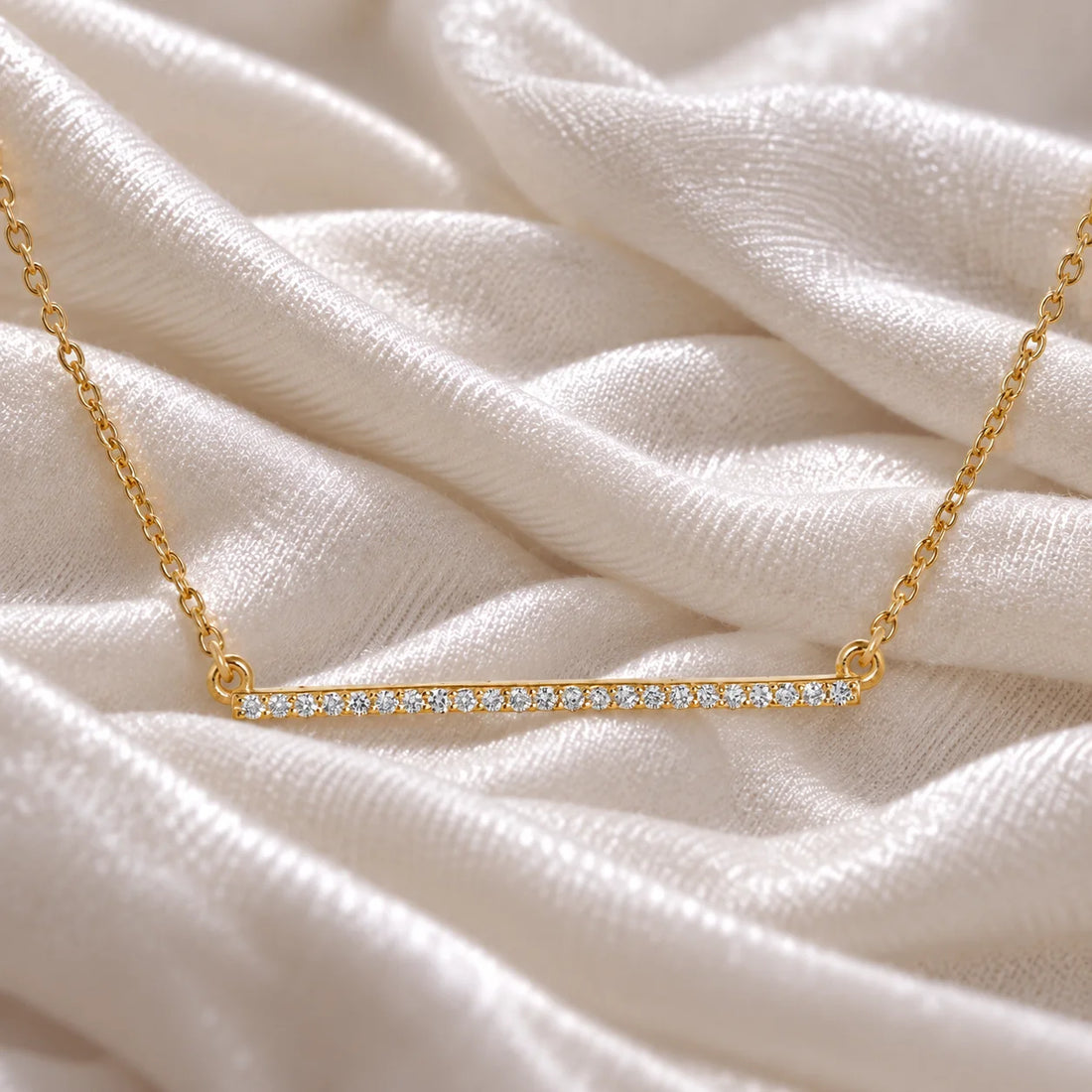 Gemstone_necklace_in_gold_plated_silver_in_a_bar_design_with_CZ_stones_at_front_angle_view_on_soft_fabric_background