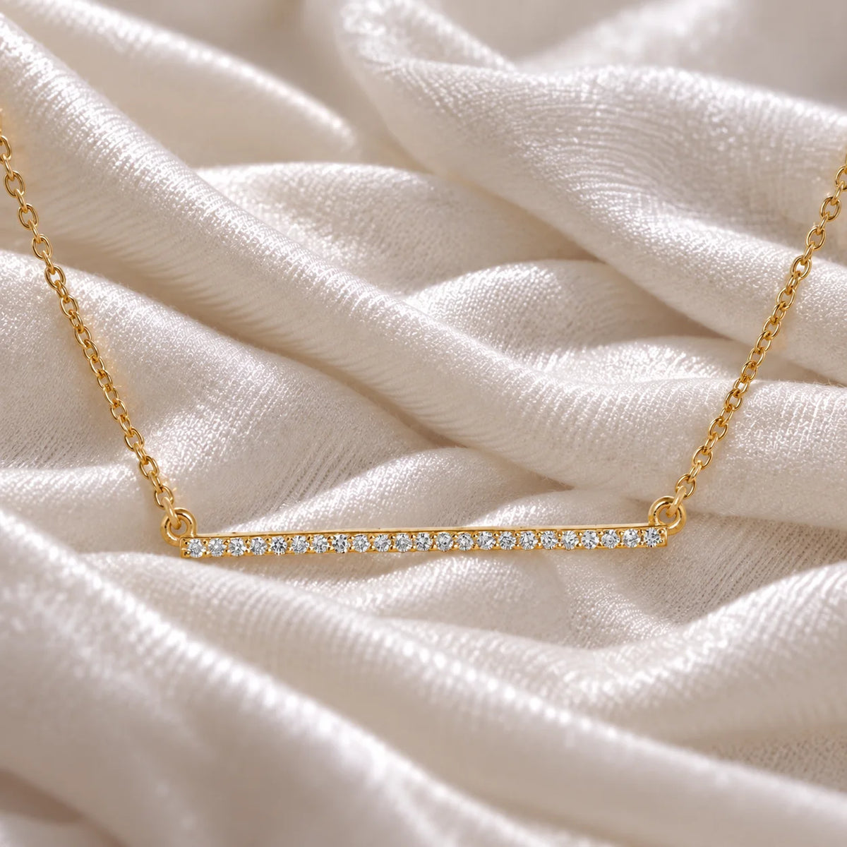 Gemstone_necklace_in_gold_plated_silver_in_a_bar_design_with_CZ_stones_at_front_angle_view_on_soft_fabric_background