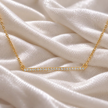 Gemstone_necklace_in_gold_plated_silver_in_a_bar_design_with_CZ_stones_at_front_angle_view_on_soft_fabric_background