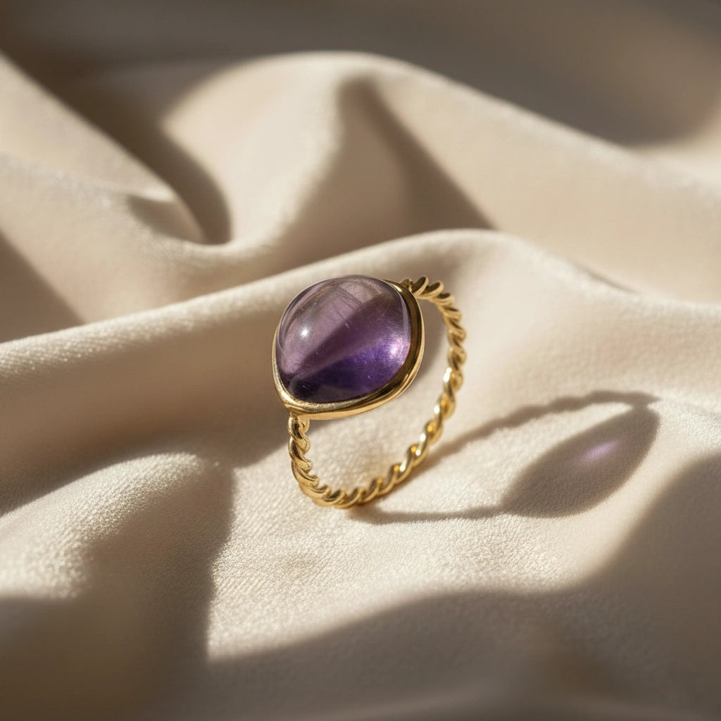 genuine amethyst ring cocktail ring shown at side angle view featuring oval purple stone with gold band on soft fabric background