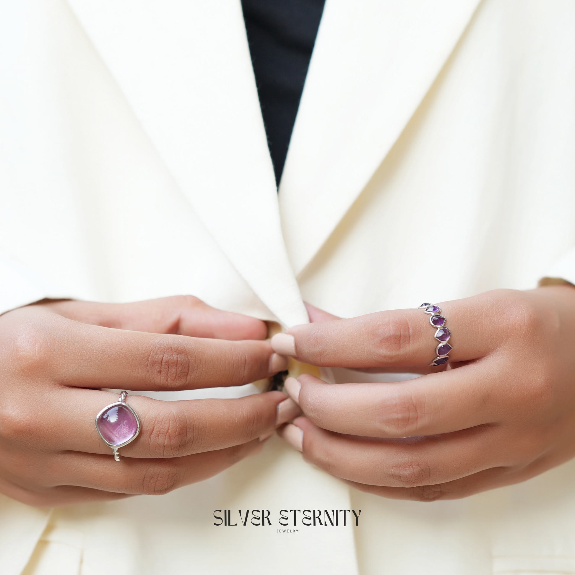 genuine amethyst ring cocktail ring shown at front angled view worn on hand while buttoning white blazer with indoor background