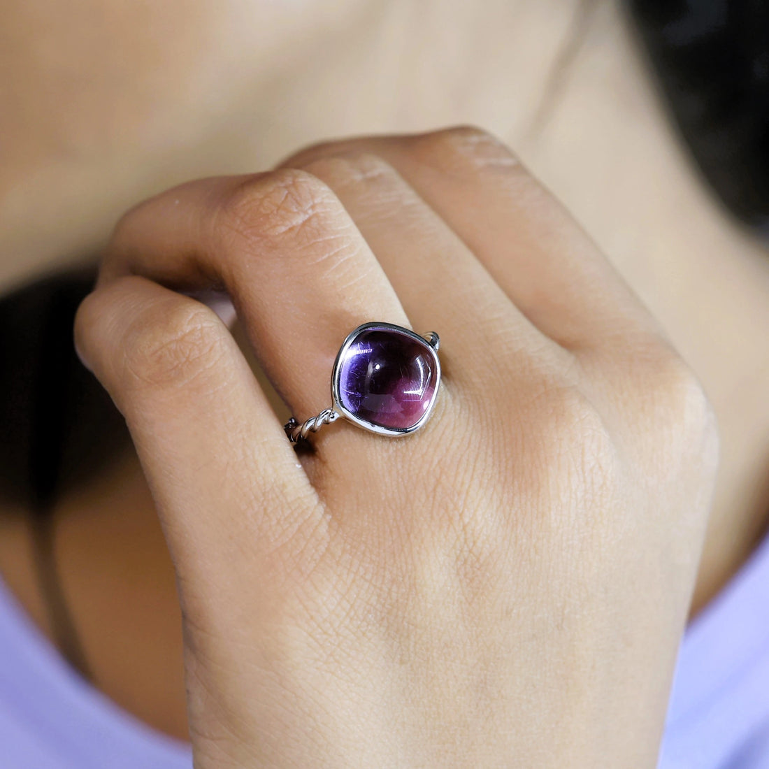 genuine amethyst ring cocktail ring shown at side angle view featuring purple stone with twisted silver band on white fabric