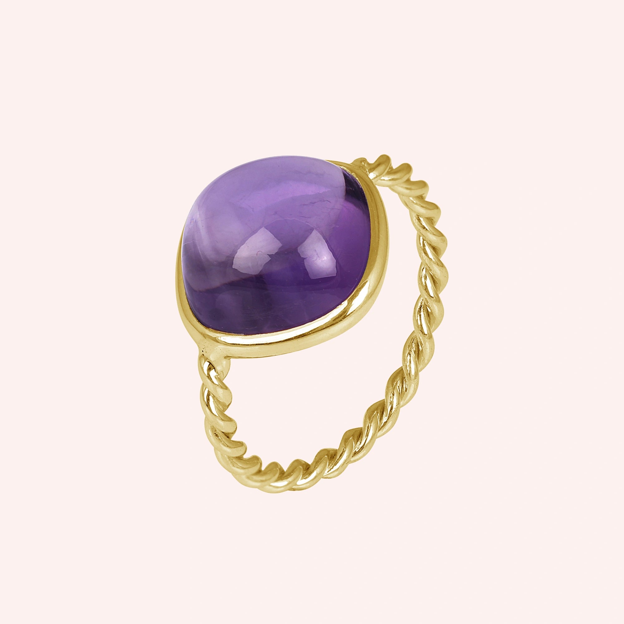 genuine amethyst ring cocktail ring shown at side angle view featuring purple stone with gold twisted band on a pink background
