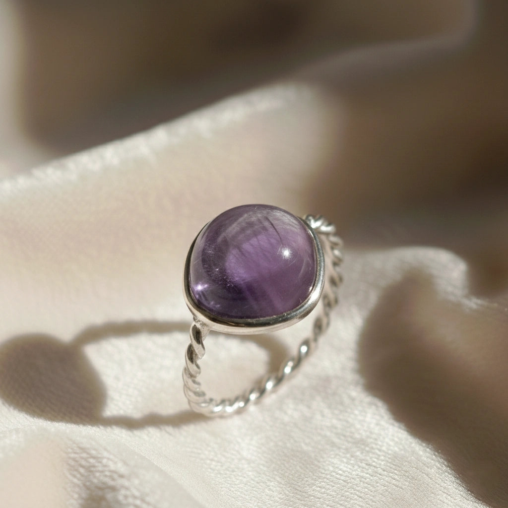 genuine amethyst ring cocktail ring shown at side angle view featuring purple stone with twisted silver band on white fabric