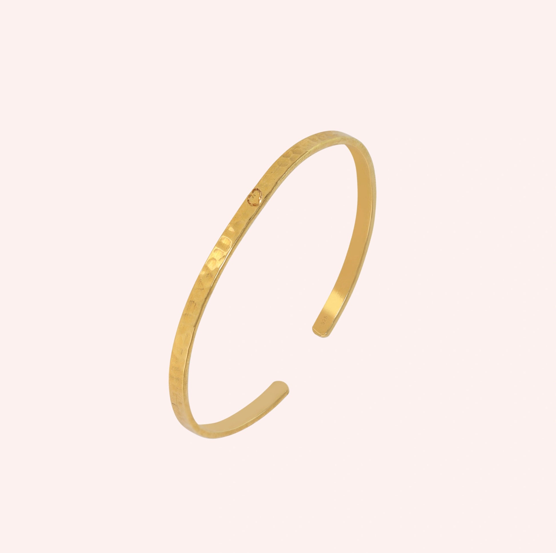 Gold_cuff_bracelet_in_gold_plated_silver_with_an_engraved_heart_at_slight_angle_view_on_solid_pink_background