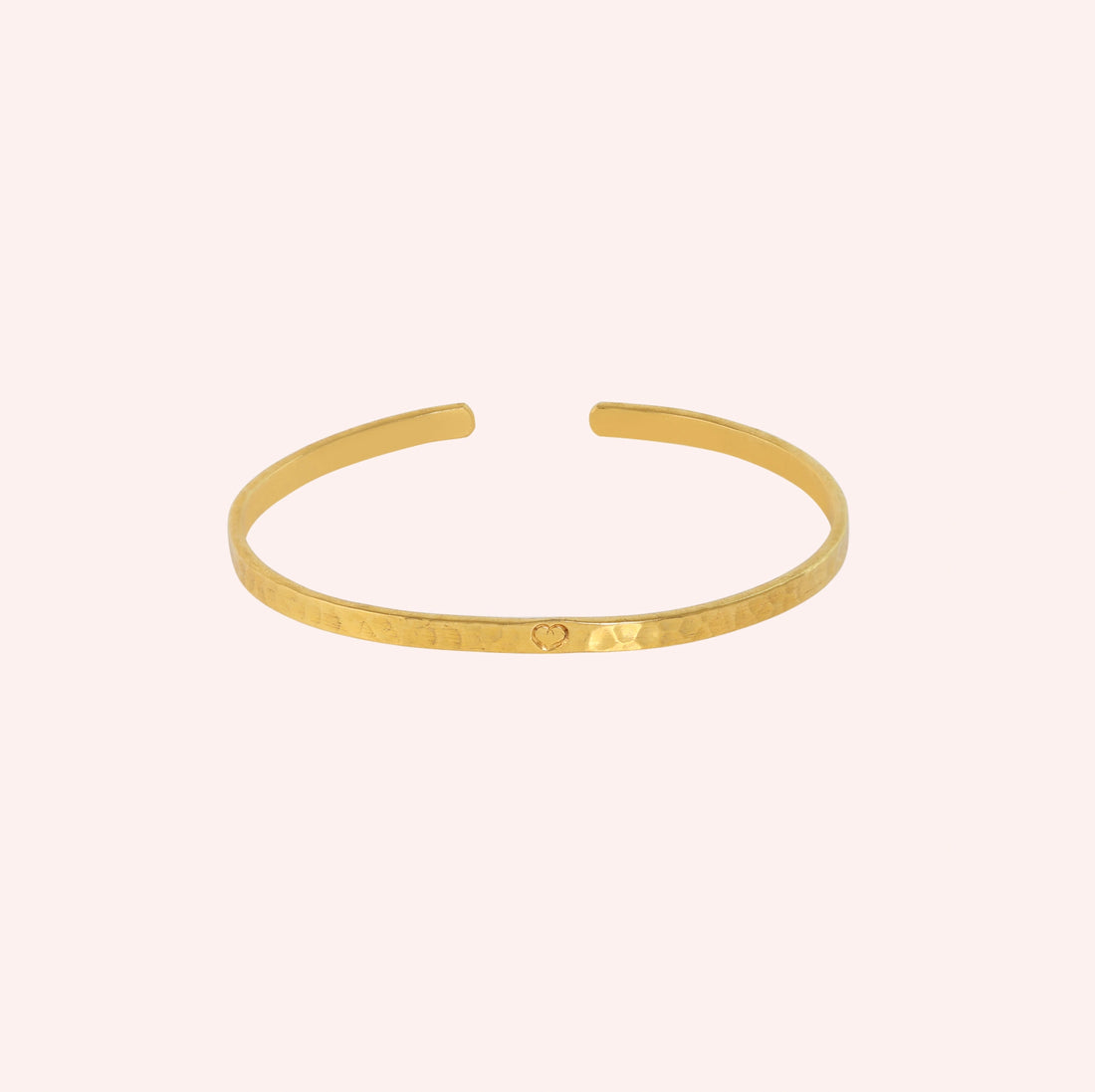 Gold_cuff_bracelet_in_gold_plated_silver_with_an_engraved_heart_at_front_angle_view_on_solid_pink_background