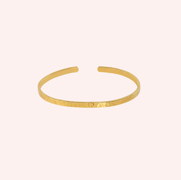 Gold_cuff_bracelet_in_gold_plated_silver_with_an_engraved_heart_at_front_angle_view_on_solid_pink_background