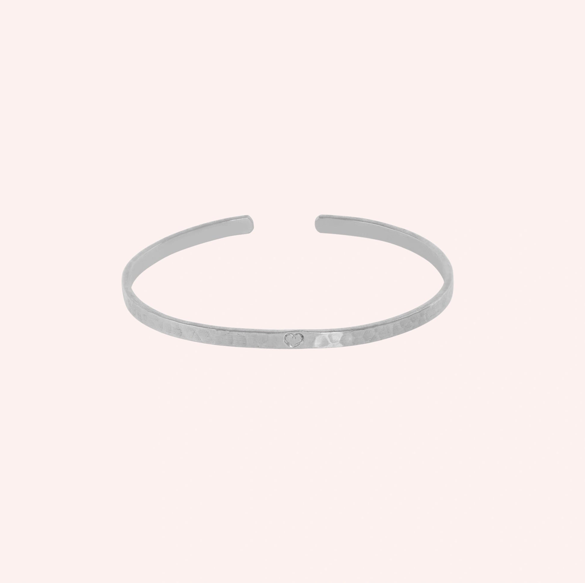 Gold_cuff_bracelet_in_sterling_silver_with_an_engraved_heart_at_slight_angle_view_on_solid_pink_background