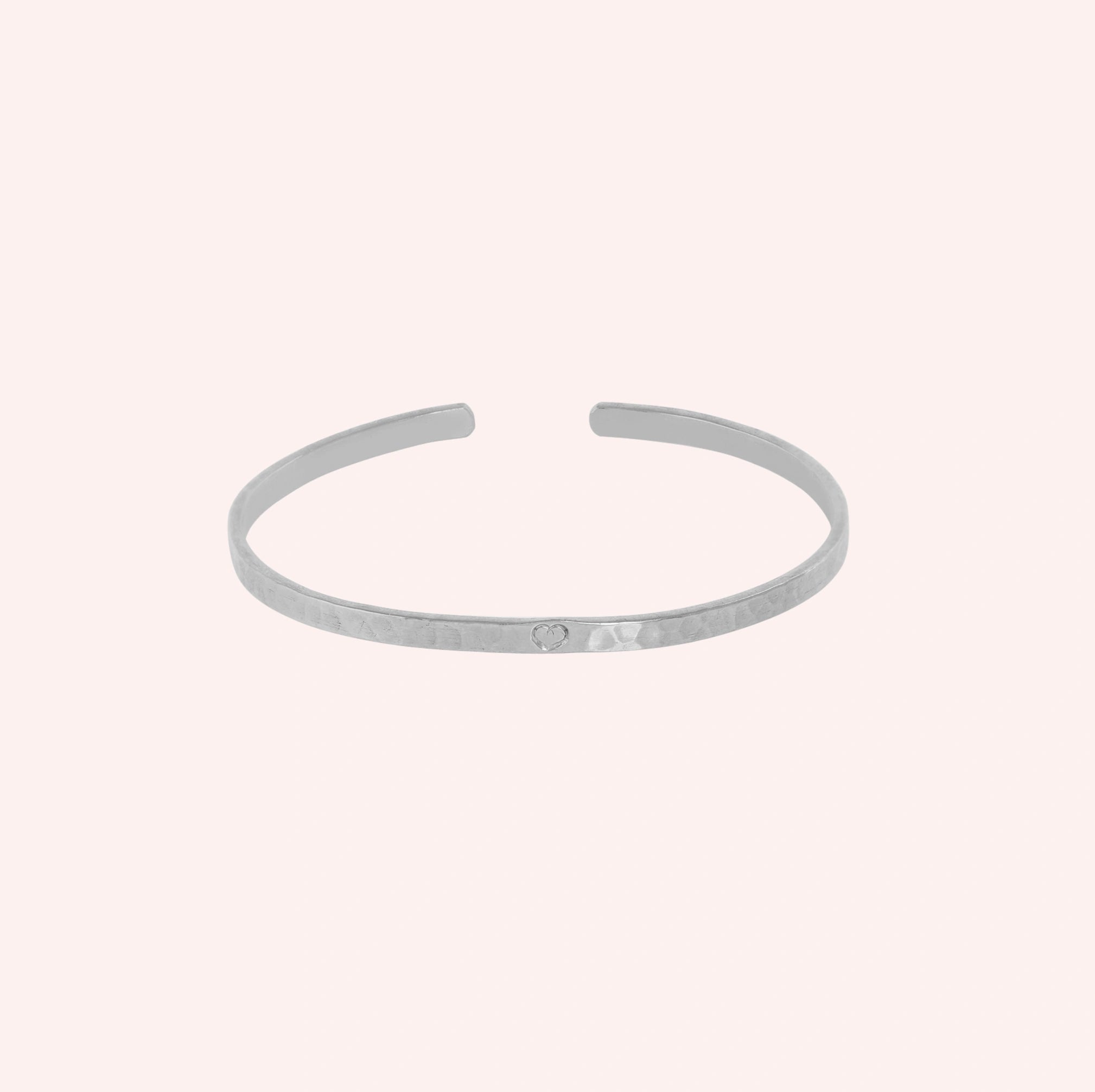 Gold_cuff_bracelet_in_sterling_silver_with_an_engraved_heart_at_slight_angle_view_on_solid_pink_background