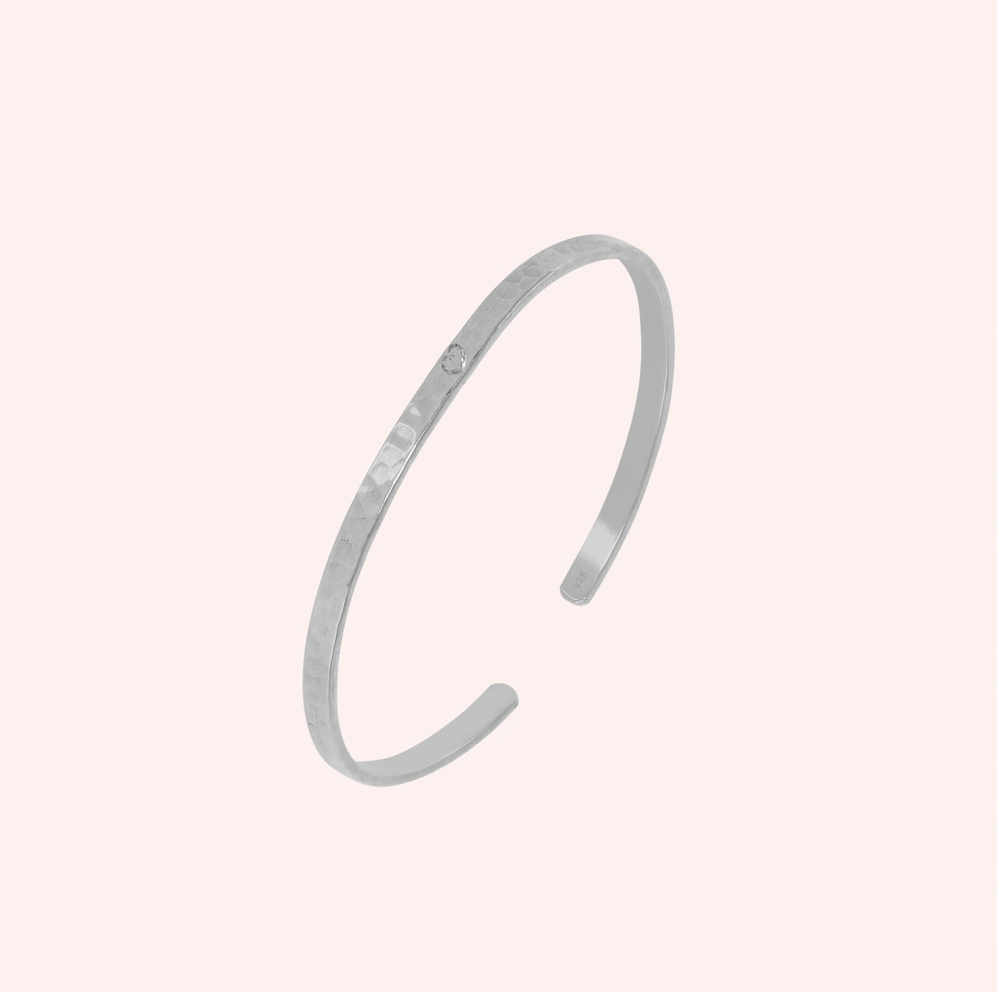 Gold_cuff_bracelet_in_sterling_silver_with_an_engraved_heart_at_slight_angle_view_on_solid_pink_background