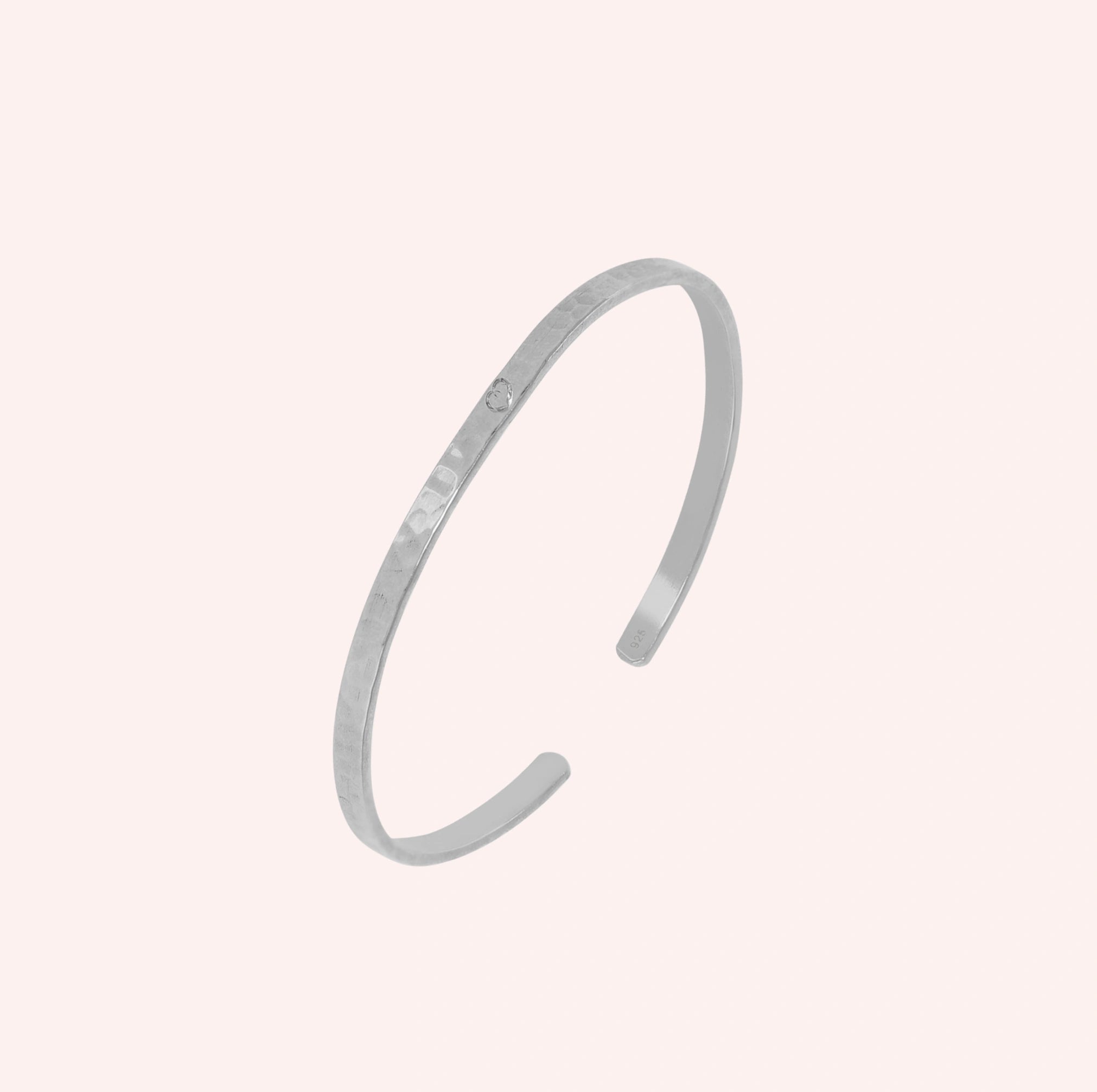 Gold_cuff_bracelet_in_sterling_silver_with_an_engraved_heart_at_slight_angle_view_on_solid_pink_background
