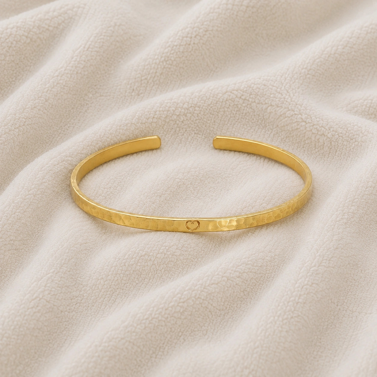 Gold_cuff_bracelet_in_gold_plated_silver_with_an_engraved_heart_at_front_angle_view_on_soft_fabric_background