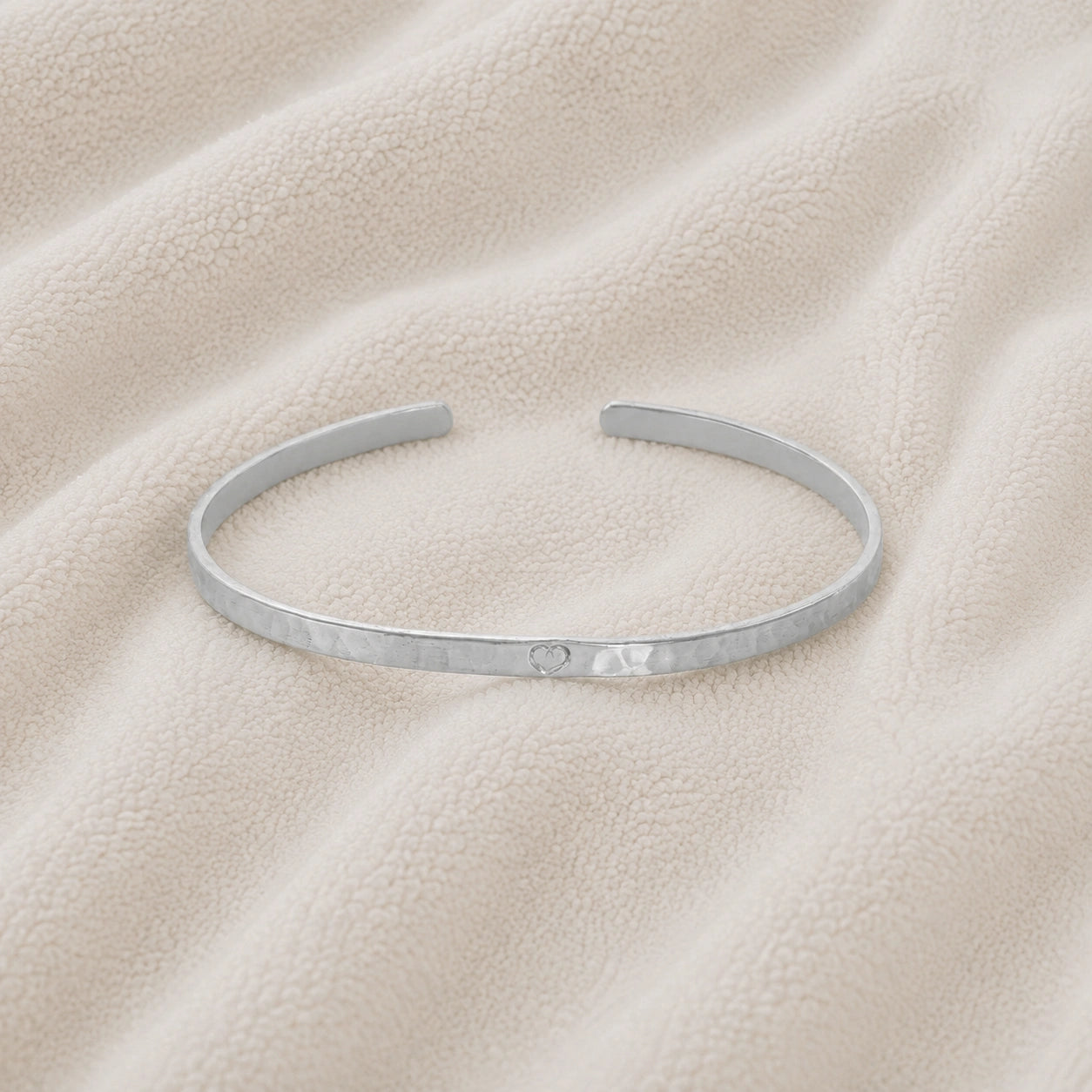 Gold_cuff_bracelet_in_sterling_silver_with_an_engraved_heart_at_front_angle_view_on_soft_fabric_background