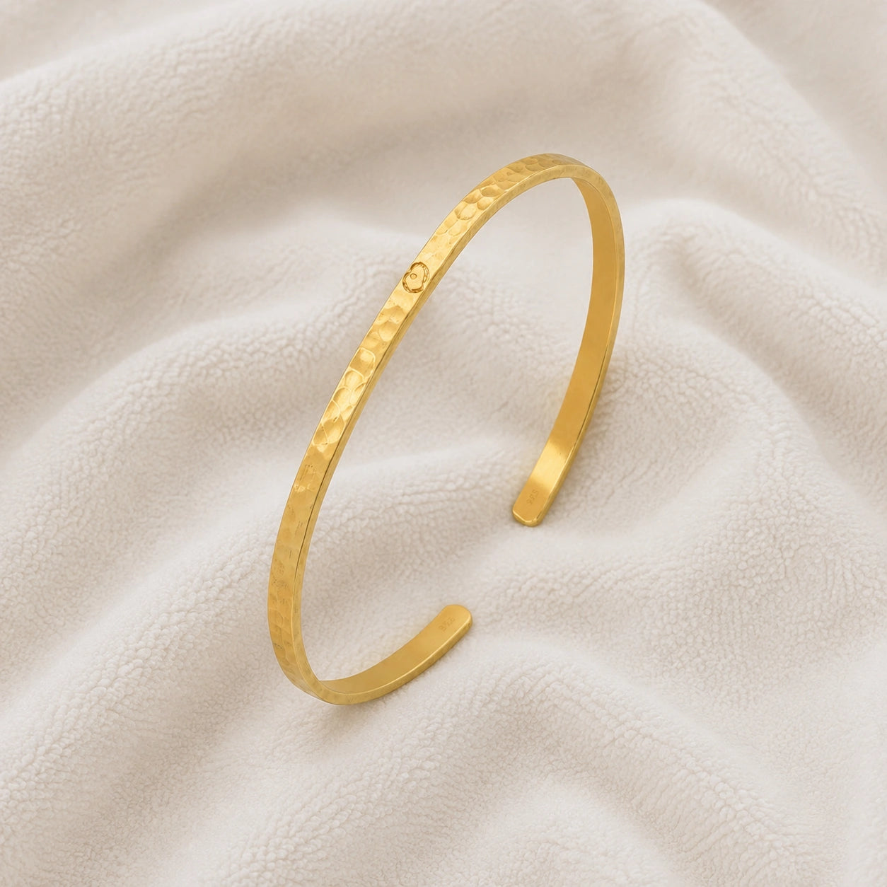 Gold_cuff_bracelet_in_gold_plated_silver_with_an_engraved_heart_at_slight_angle_view_on_soft_fabric_background