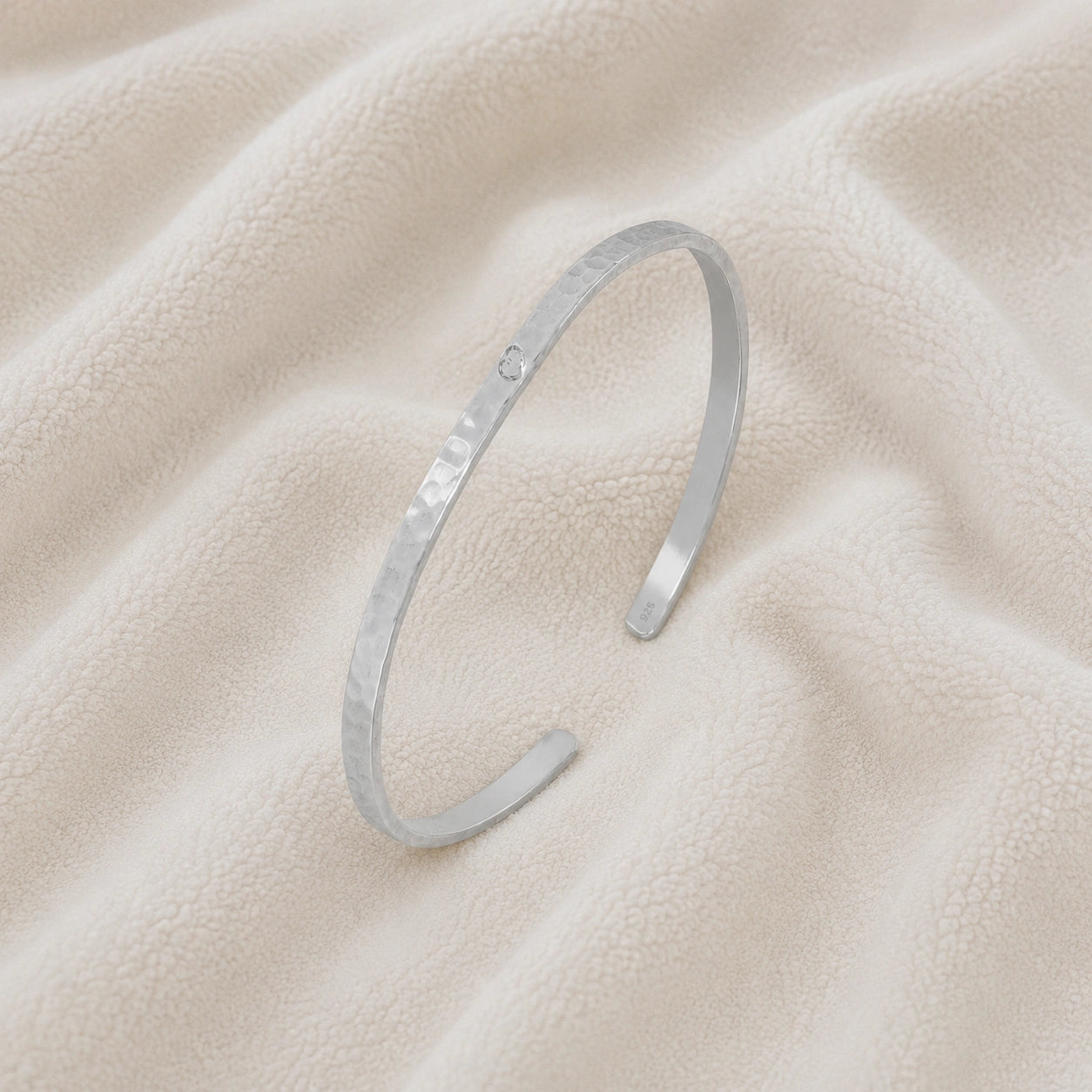 Gold_cuff_bracelet_in_sterling_silver_with_an_engraved_heart_at_slight_angle_view_on_soft_fabric_background