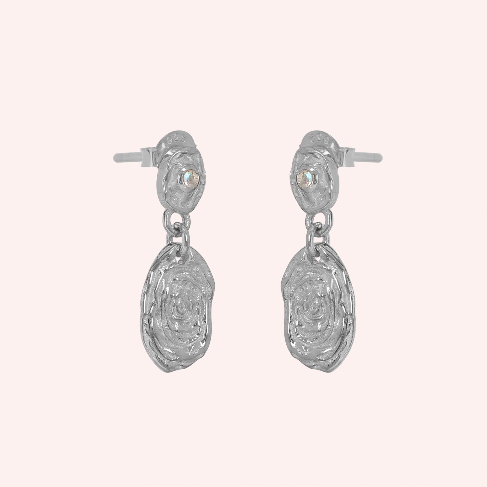 Gold_dangle_earrings_with_sterling_silver_textured_oval_charms_and_moonstone_at_side_angle_on_solid_pink_background