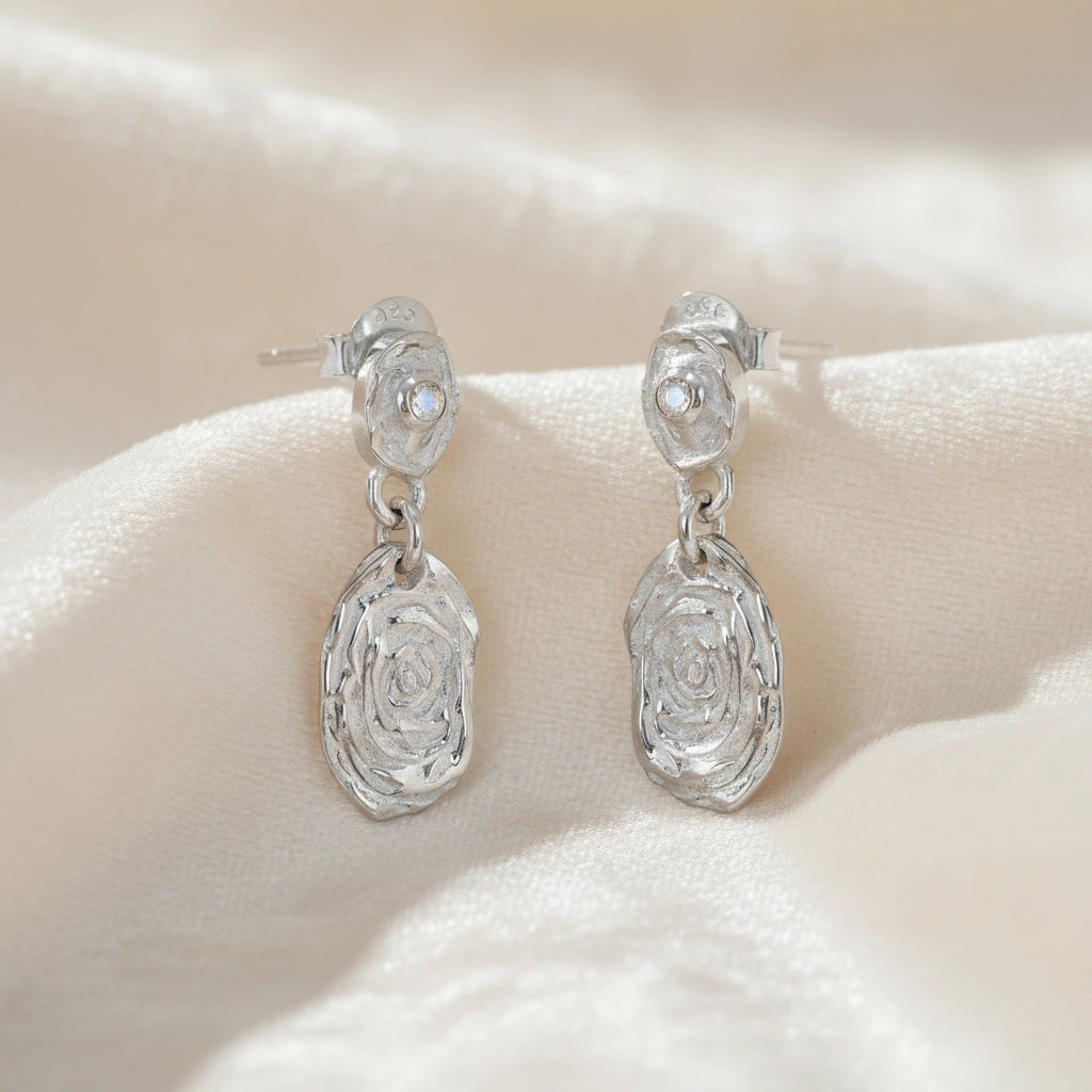 Gold_dangle_earrings_with_sterling_silver_textured_oval_charms_and_moonstone_at_side_angle_on_soft_fabric_background