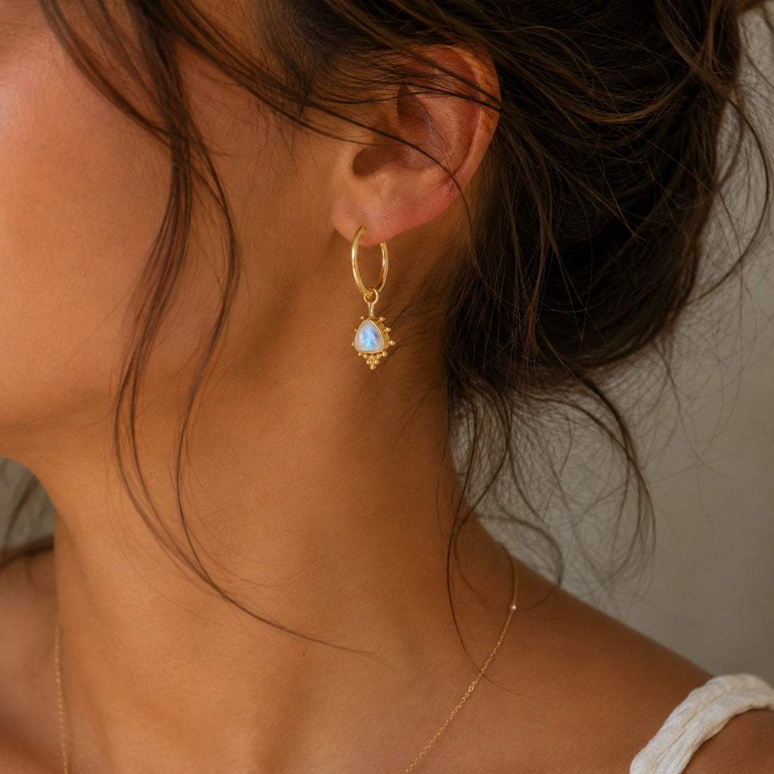 Gold_drop_earrings_in_gold_plated_silver_at_slightly_angled_with_triangle_moonstone_charms_on_soft_fabric_background