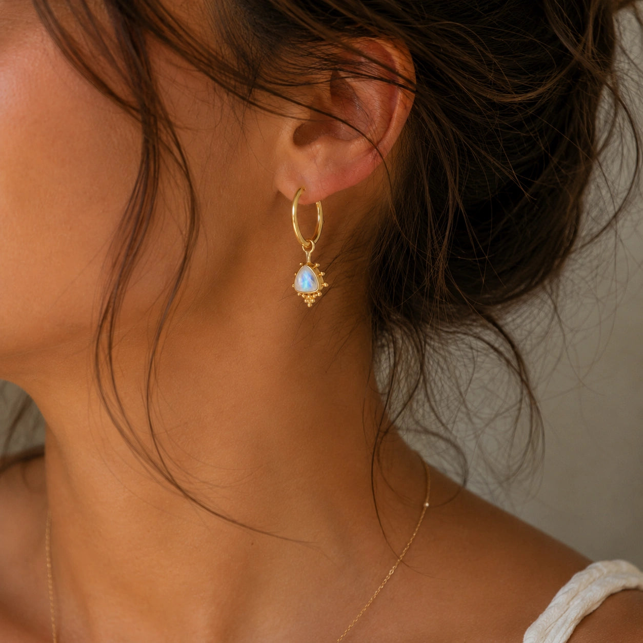 Gold_drop_earrings_in_gold_plated_silver_at_slightly_angled_with_triangle_moonstone_charms_worn_by_a_model