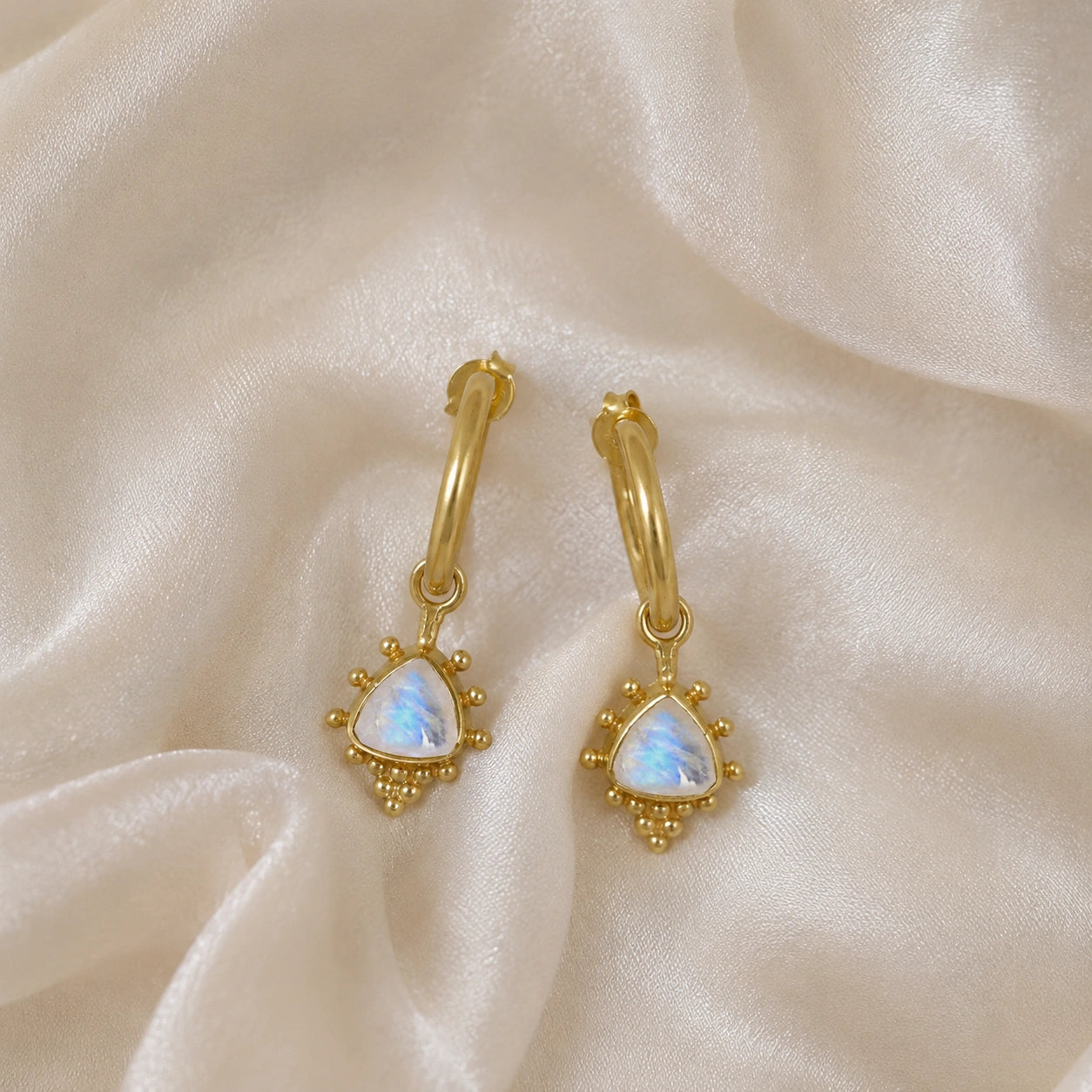 Gold_drop_earrings_in_gold_plated_silver_at_front_angle_with_triangle_moonstone_charms_on_soft_fabric_background