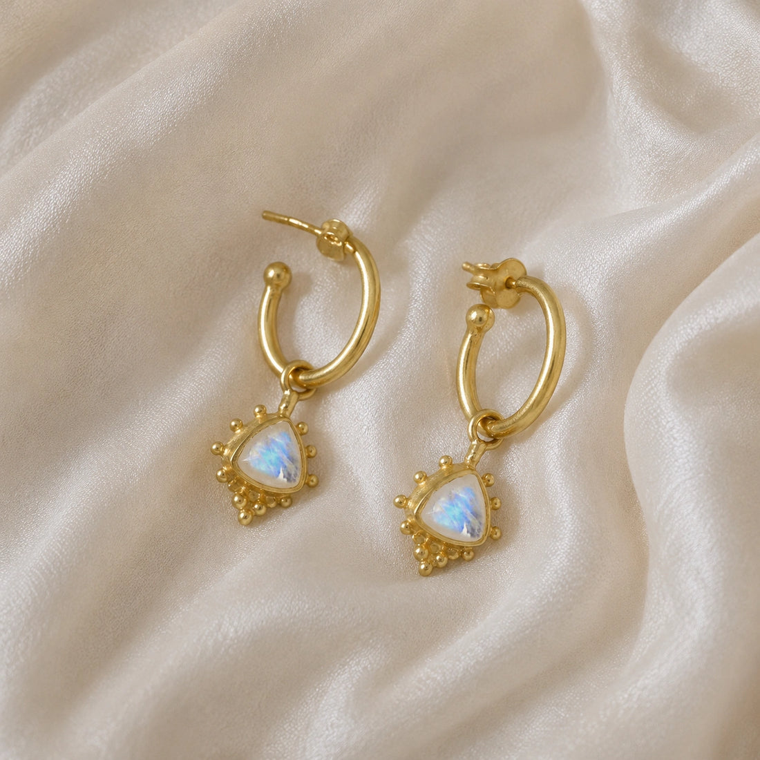 Gold_drop_earrings_in_gold_plated_silver_at_slightly_angled_with_triangle_moonstone_charms_on_soft_fabric_background