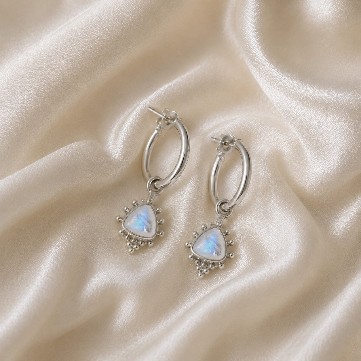 Gold_drop_earrings_in_sterling_silver_at_front_angle_with_triangle_moonstone_charms_on_soft_fabric_background