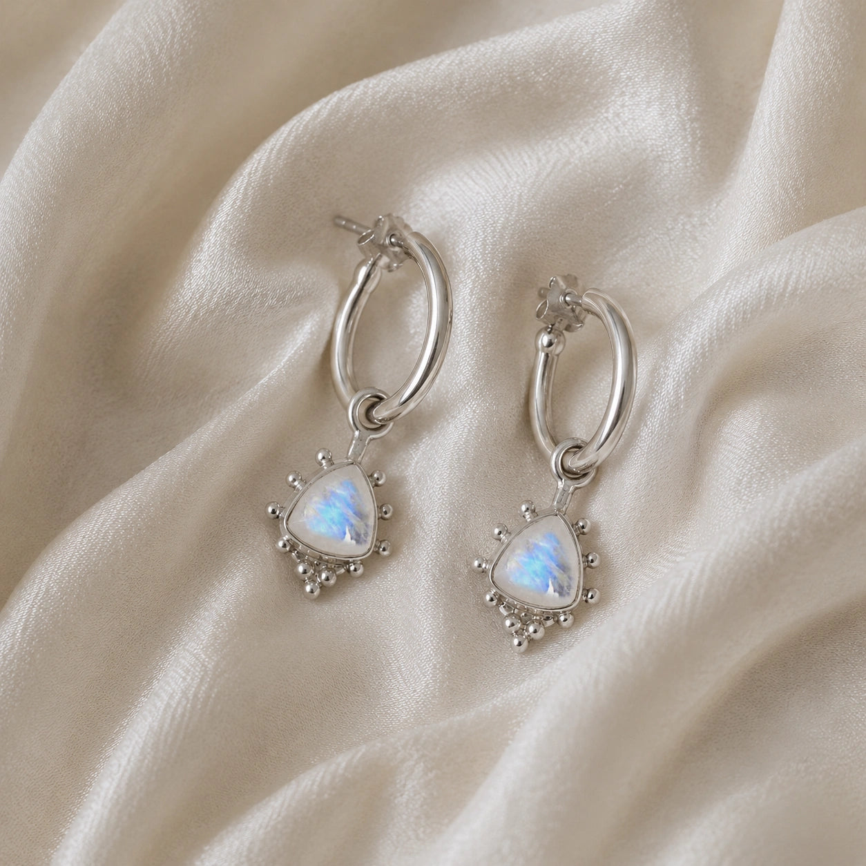 Gold_drop_earrings_in_sterling_silver_at_slightly_angled_with_triangle_moonstone_charms_on_soft_fabric_background