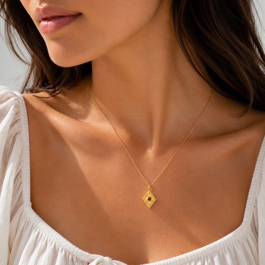Gold_locket_necklace_gold_plated_silver_slightly_angle_with_textured_diamond_pendant_and_garnet_center_stone_on_soft_fabric_background