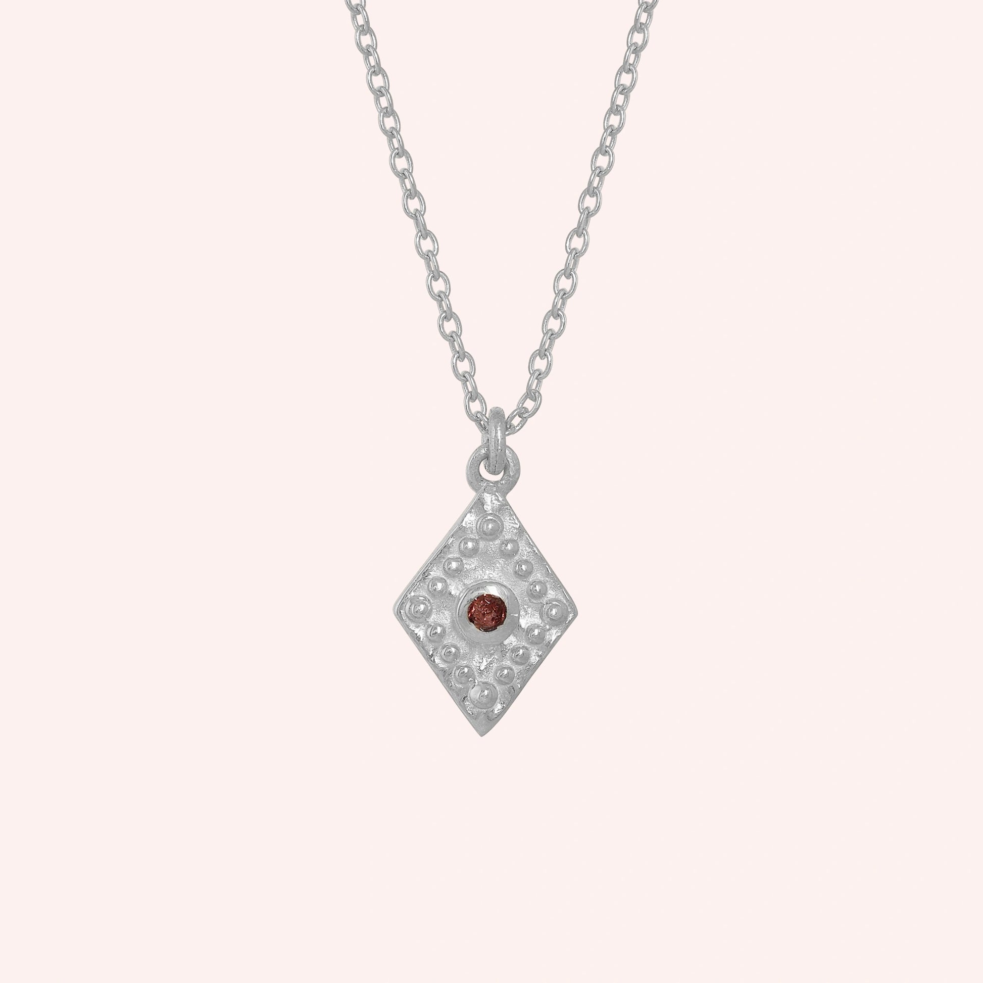 Gold_locket_necklace_sterling_silver_front_angle_with_textured_diamond_pendant_and_garnet_center_stone_on_solid_pink_background