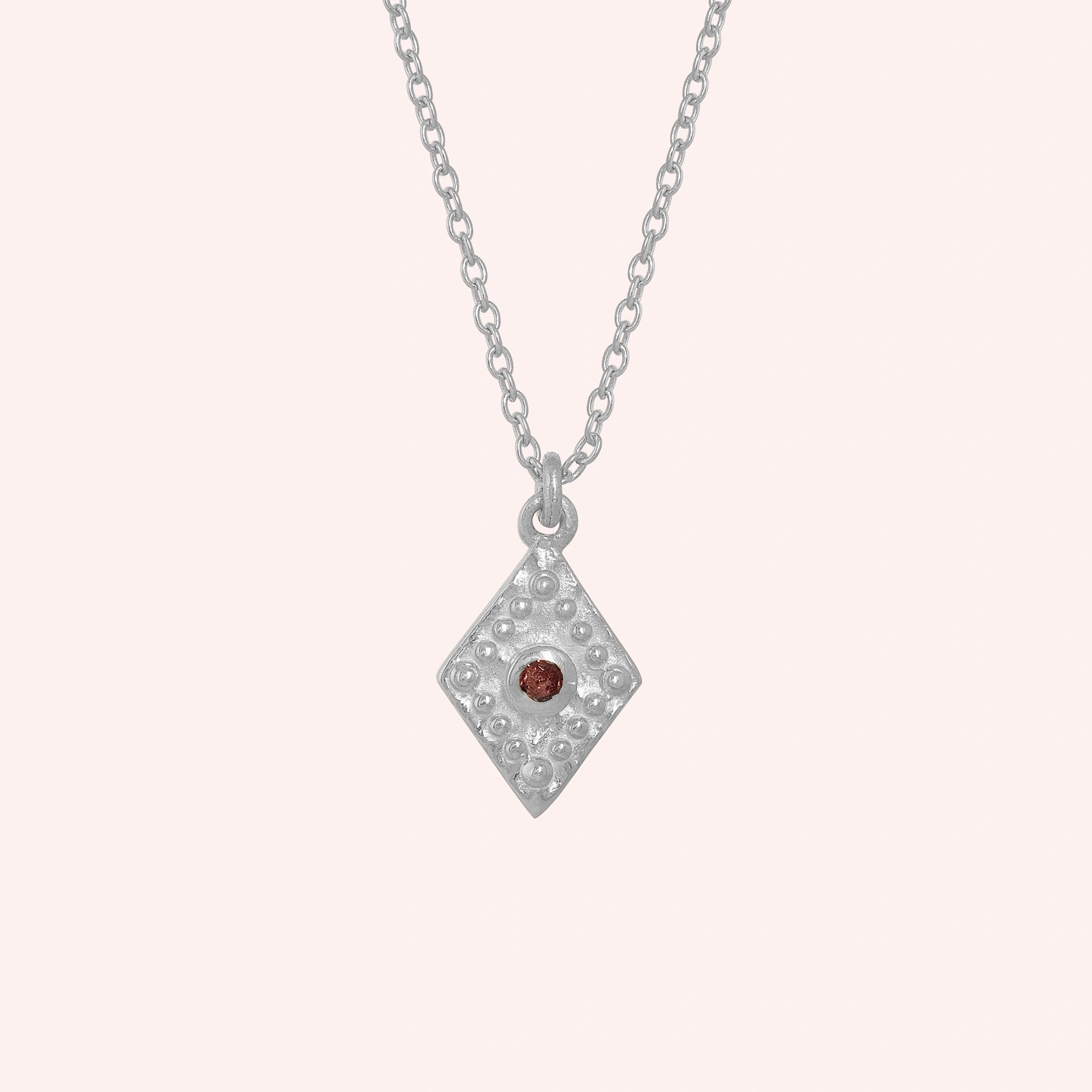 Gold_locket_necklace_sterling_silver_front_angle_with_textured_diamond_pendant_and_garnet_center_stone_on_solid_pink_background