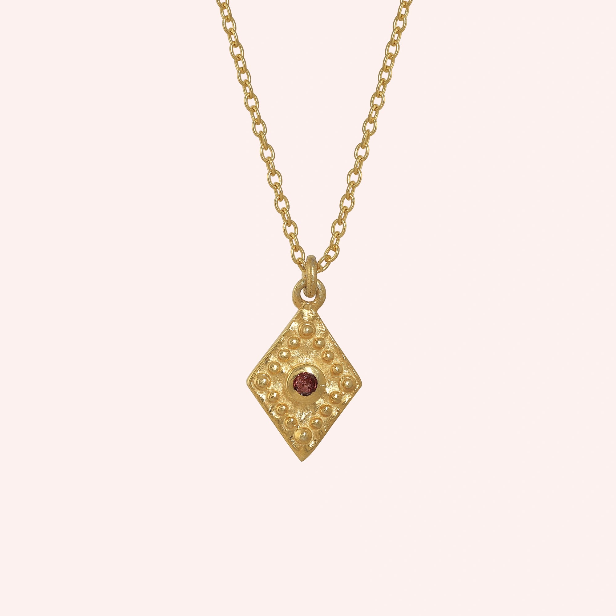 Gold_locket_necklace_gold_plated_silver_front_angle_with_textured_diamond_pendant_and_garnet_center_stone_on_solid_pink_background