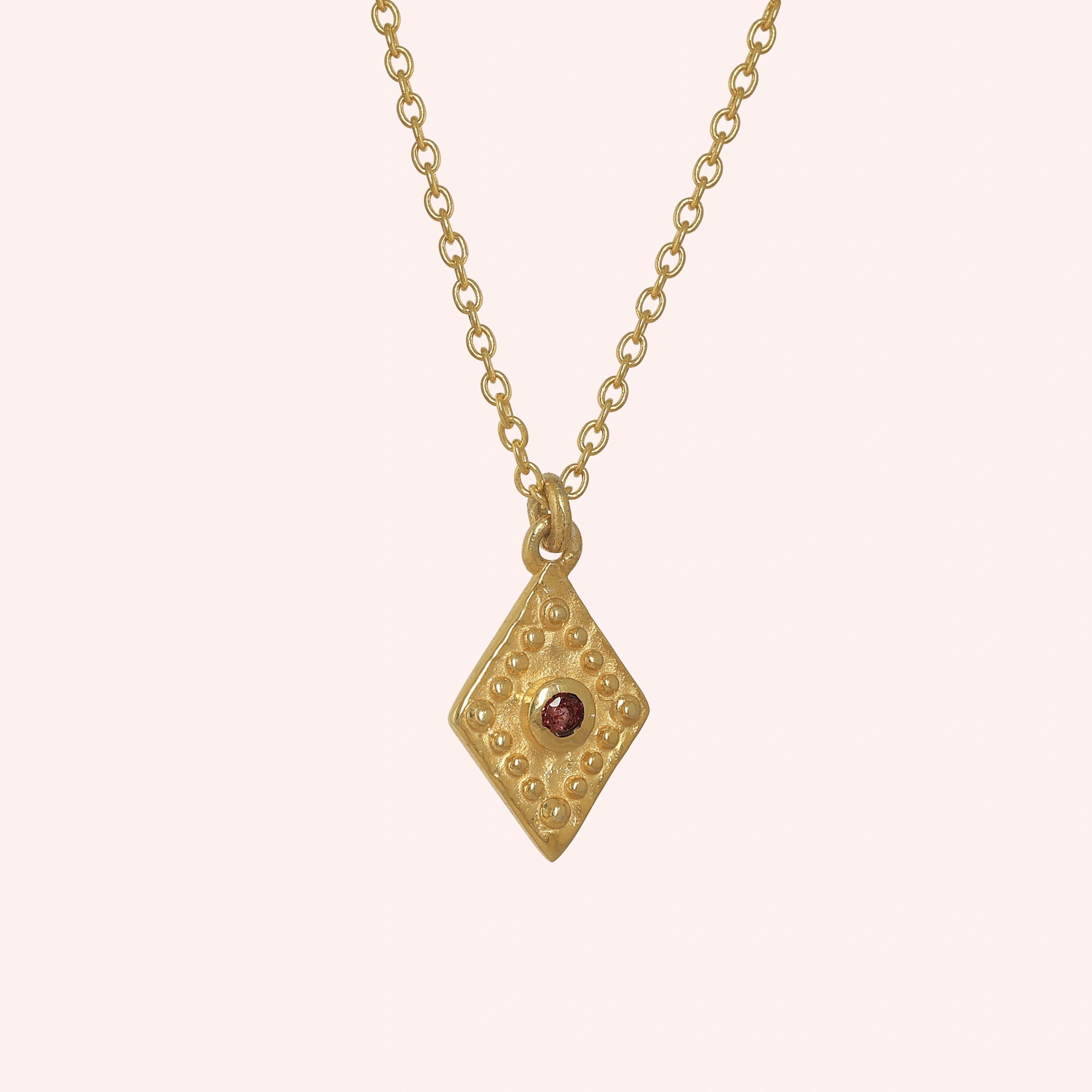 Gold_locket_necklace_gold_plated_silver_slightly_angled_with_textured_diamond_pendant_and_garnet_center_stone_on_solid_pink_background