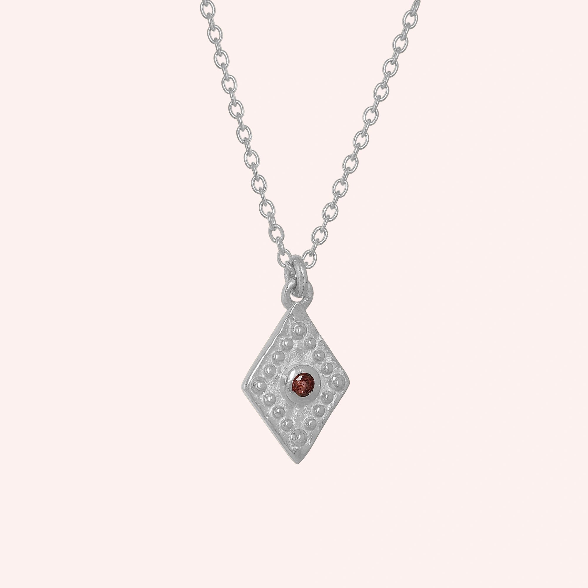 Gold_locket_necklace_sterling_silver_slightly_angled_with_textured_diamond_pendant_and_garnet_center_stone_on_solid_pink_background