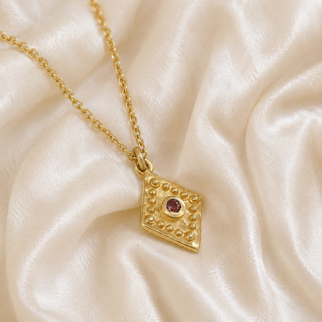 Gold_locket_necklace_gold_plated_silver_slightly_angle_with_textured_diamond_pendant_and_garnet_center_stone_on_soft_fabric_background
