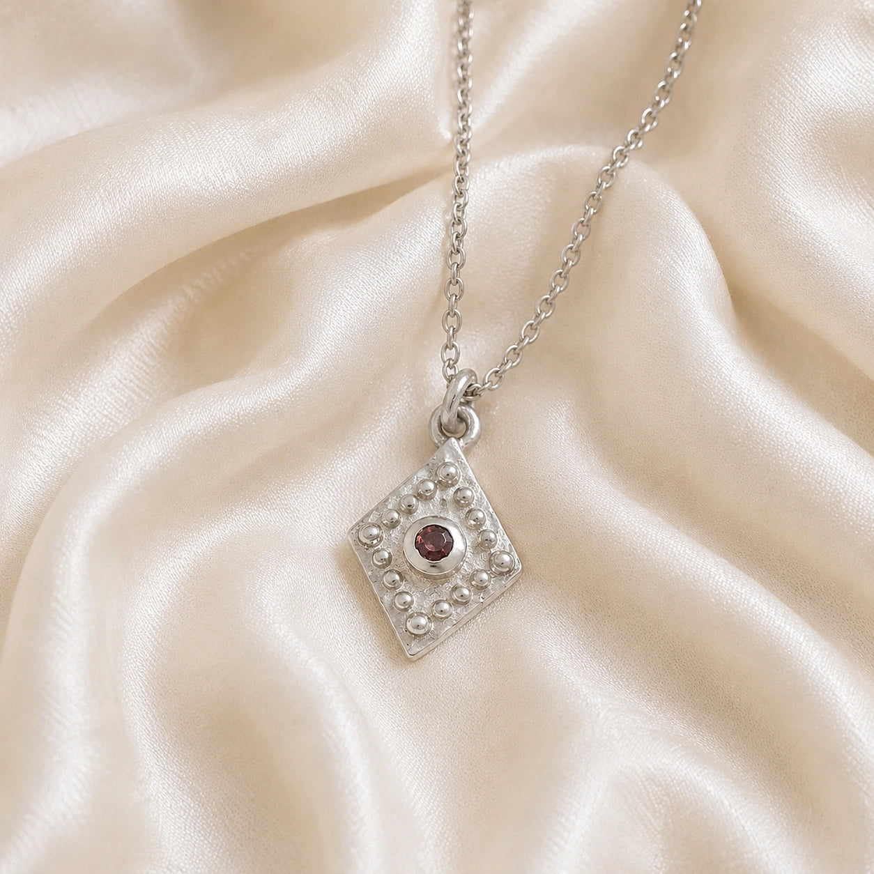 Gold_locket_necklace_sterling_silver_slightly_angled_with_textured_diamond_pendant_and_garnet_center_stone_on_soft_fabric_background