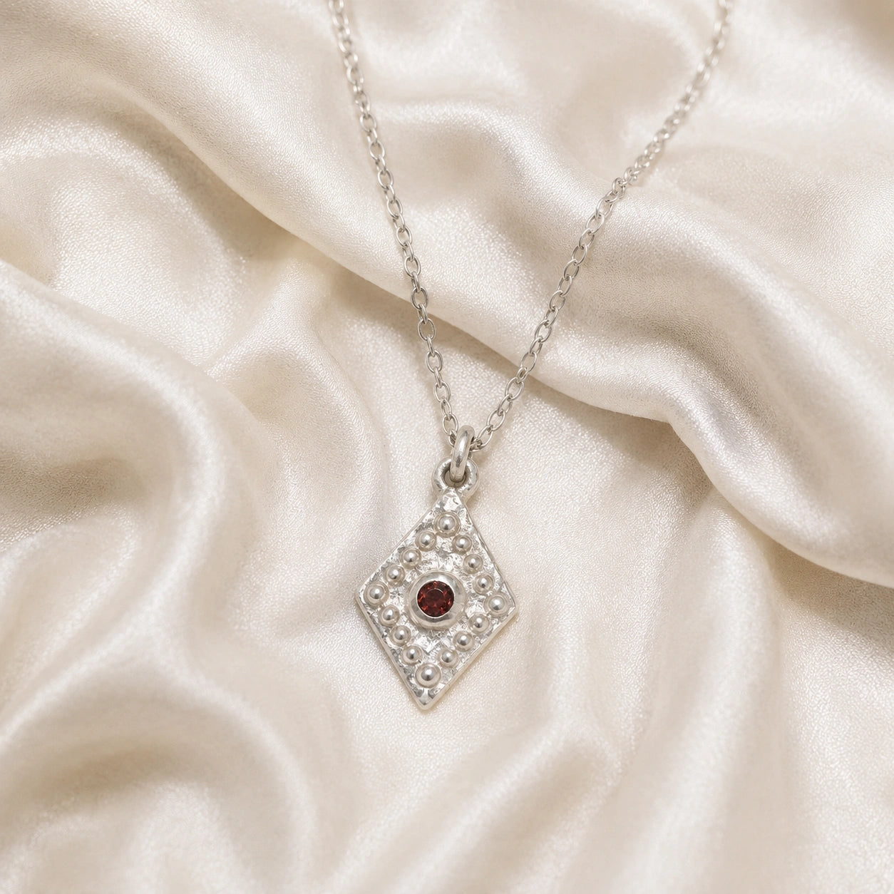 Gold_locket_necklace_sterling_silver_front_angle_with_textured_diamond_pendant_and_garnet_center_stone_on_soft_fabric_background