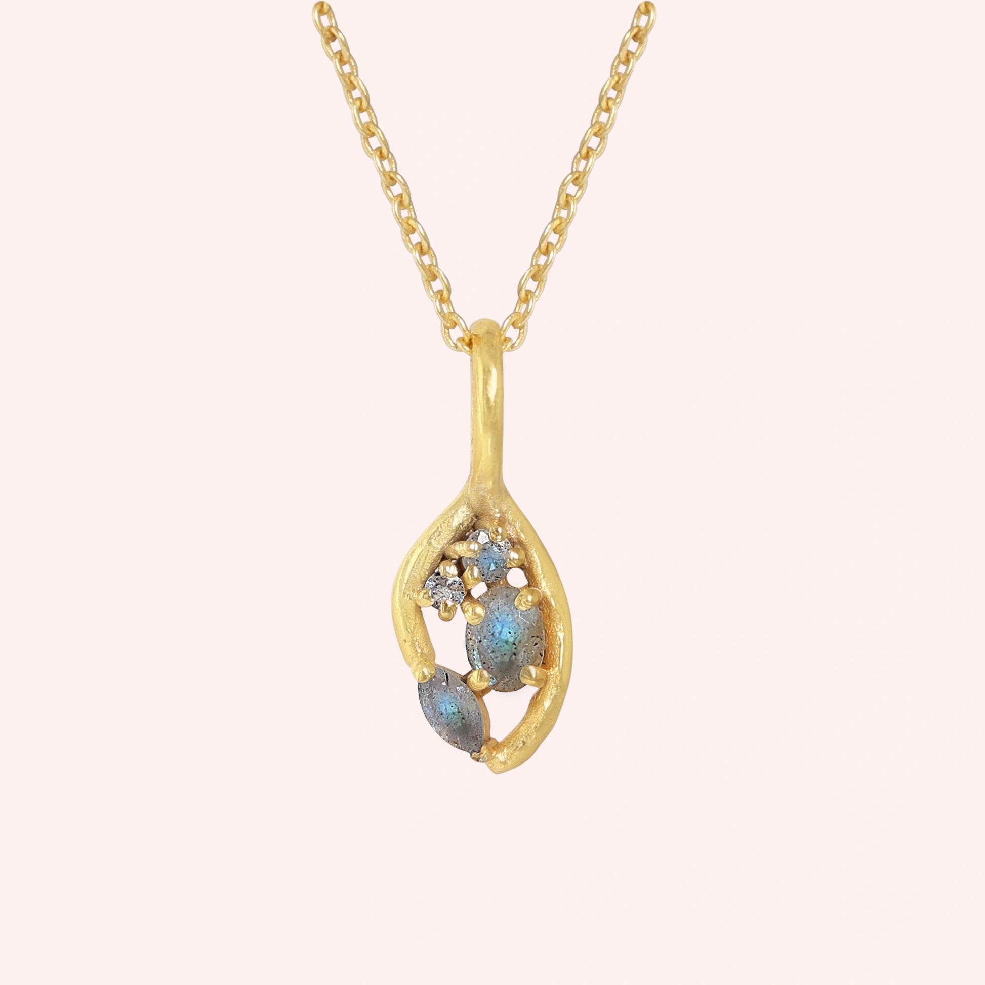 Gold_pendant_necklace_gold_plated_on_front_angle_with_labradorite_gemstones_and_floral_details_on_solid_pink_background