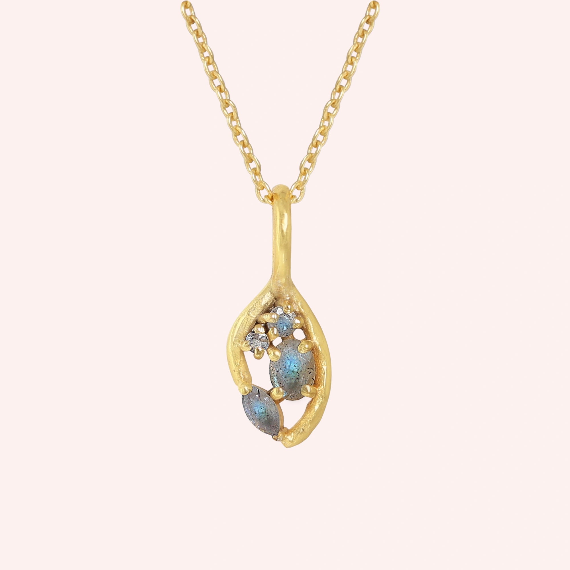 Gold_pendant_necklace_gold_plated_on_front_angle_with_labradorite_gemstones_and_floral_details_on_solid_pink_background