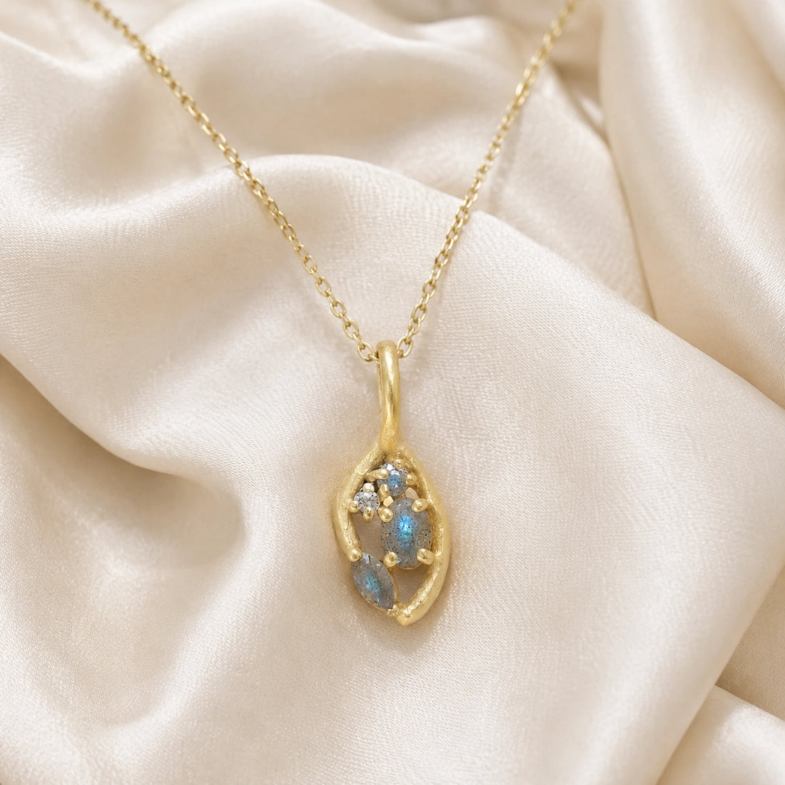 Gold_pendant_necklace_gold_plated_on_front_angle_with_labradorite_gemstones_and_floral_details_on_soft_fabric_background