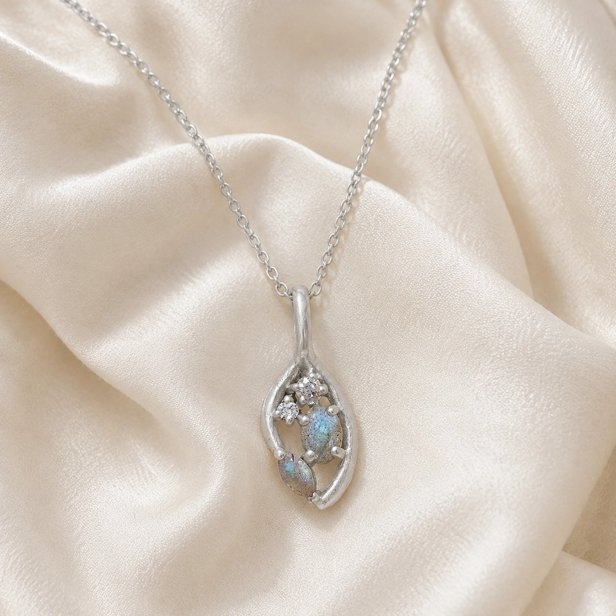 Gold_pendant_necklace_sterling_silver_on_front_angle_with_labradorite_gemstones_and_floral_details_on_soft_fabric_background