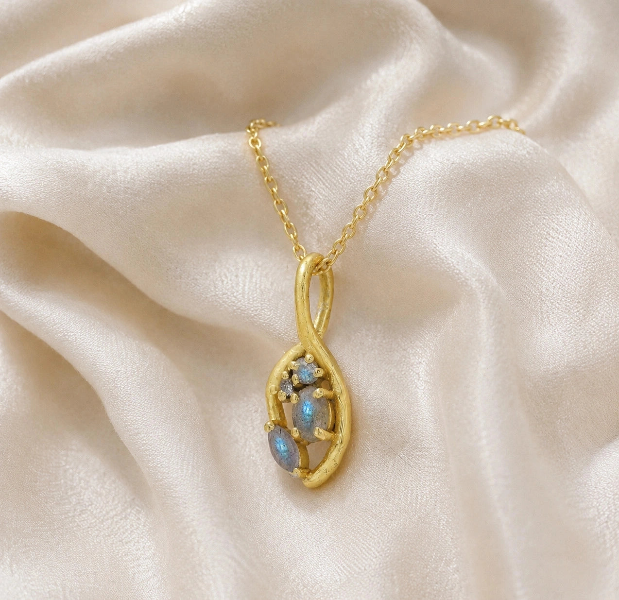 Gold_pendant_necklace_gold_plated_silver_on_slightly_angled_with_labradorite_gemstones_and_floral_details_on_soft_fabric_background