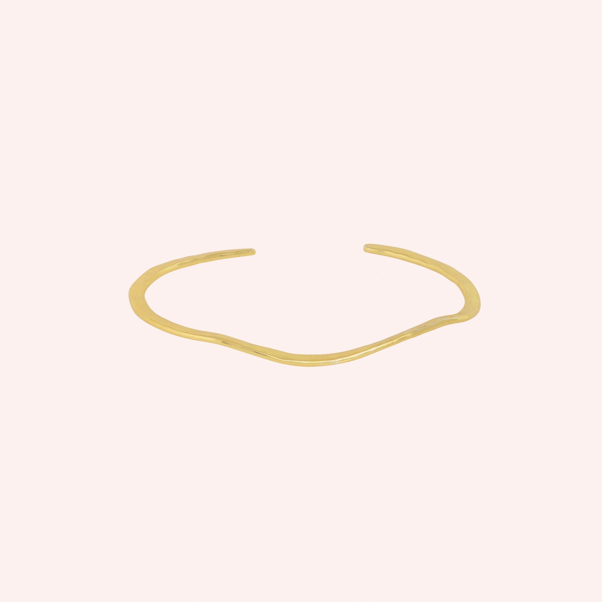Gold_plated_bracelet_in_gold_plated_silver_with_textured_wavy_band_at_front_angle_view_on_solid_pink_background