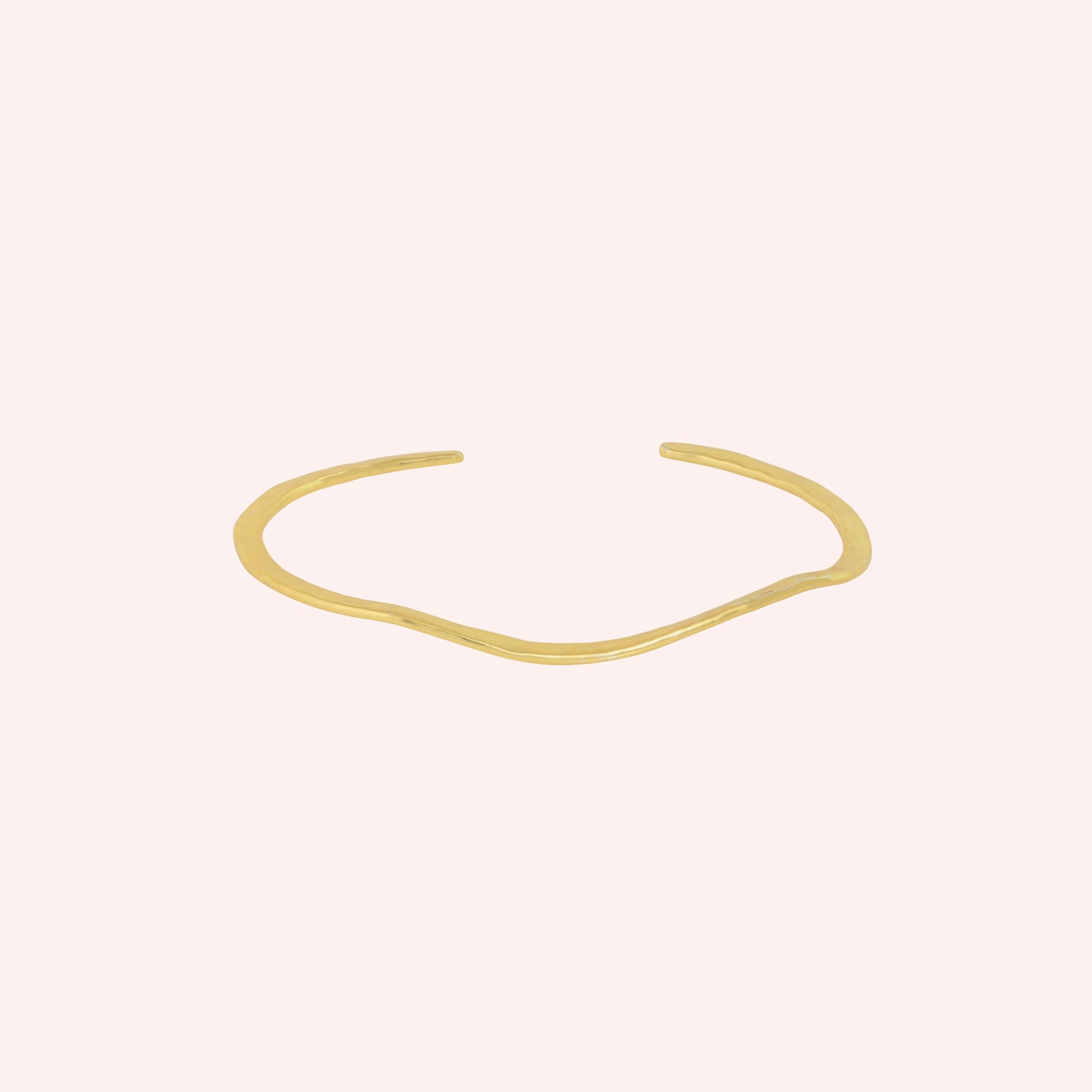 Gold_plated_bracelet_in_gold_plated_silver_with_textured_wavy_band_at_front_angle_view_on_solid_pink_background