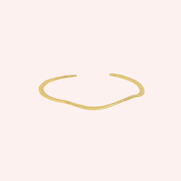 Gold_plated_bracelet_in_gold_plated_silver_with_textured_wavy_band_at_front_angle_view_on_solid_pink_background