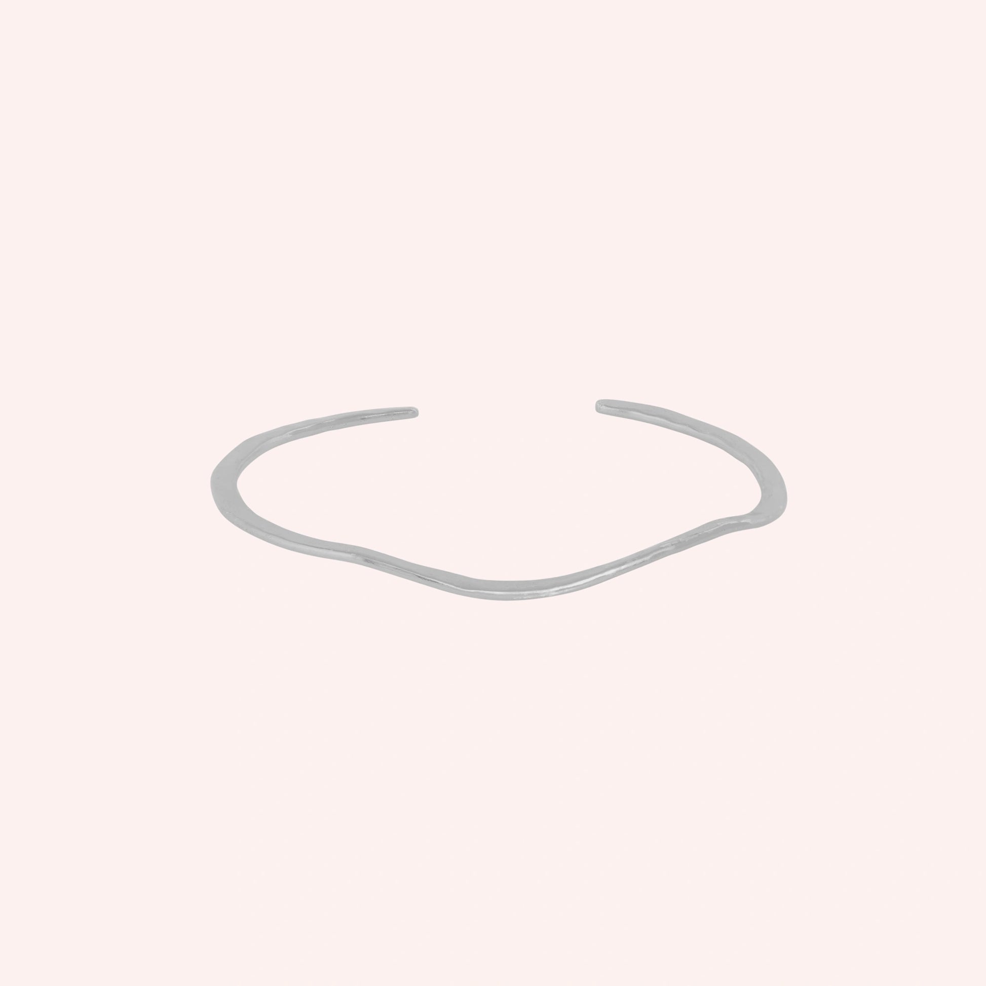 Gold_plated_bracelet_in_sterling_silver_with_textured_wavy_band_at_front_angle_view_on_solid_pink_background