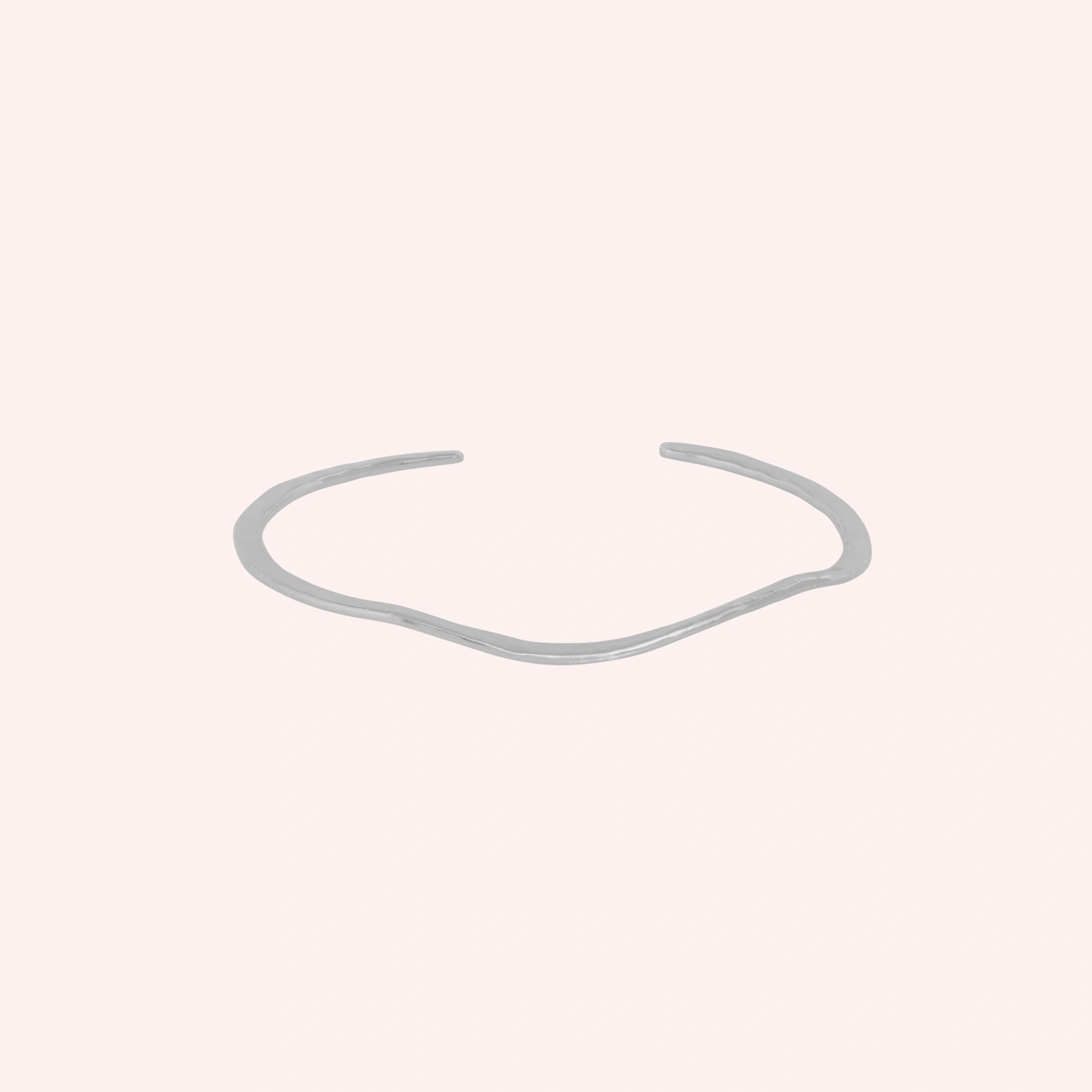 Gold_plated_bracelet_in_sterling_silver_with_textured_wavy_band_at_front_angle_view_on_solid_pink_background