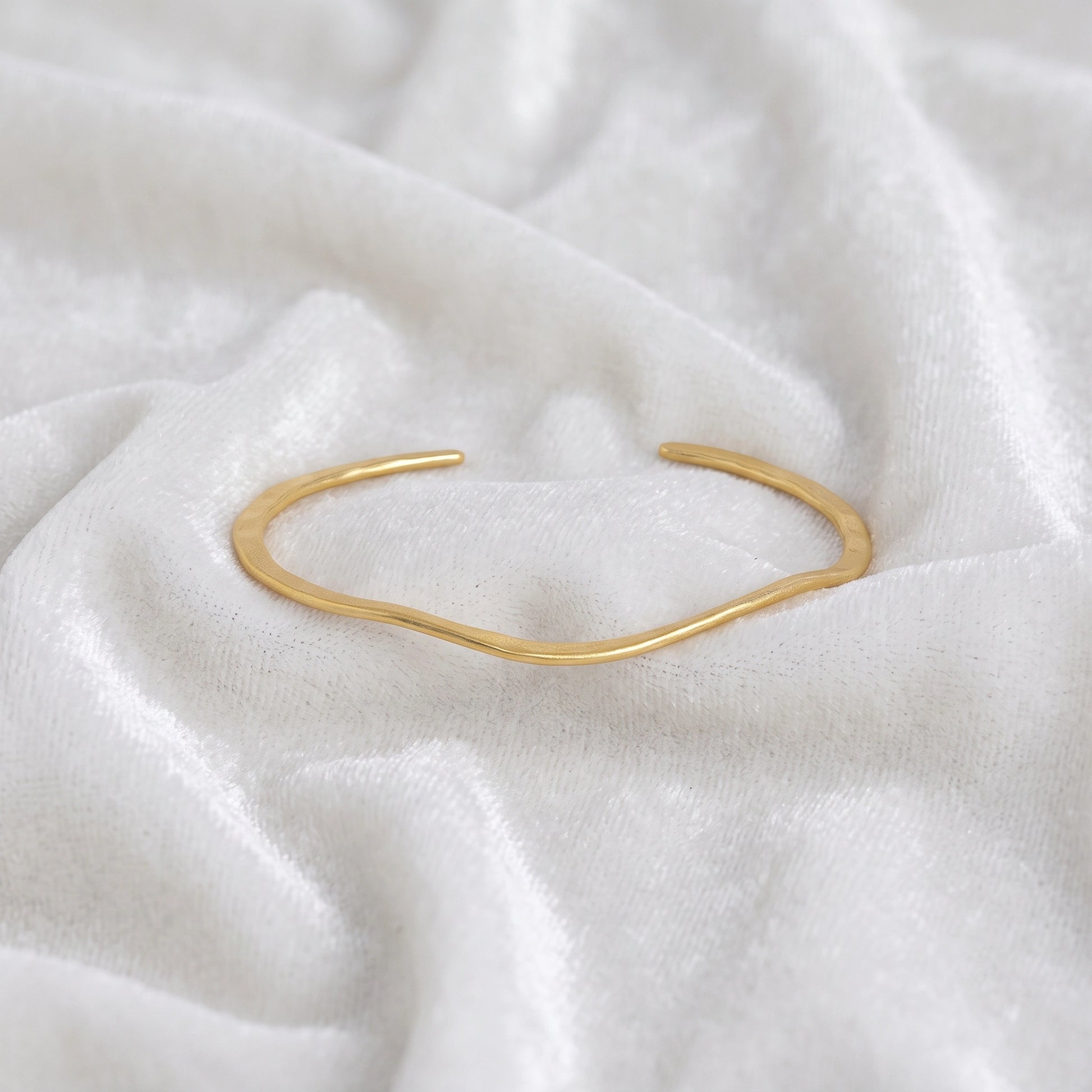 Gold_plated_bracelet_in_gold_plated_silver_with_textured_wavy_band_at_front_angle_view_on_soft_fabric_background