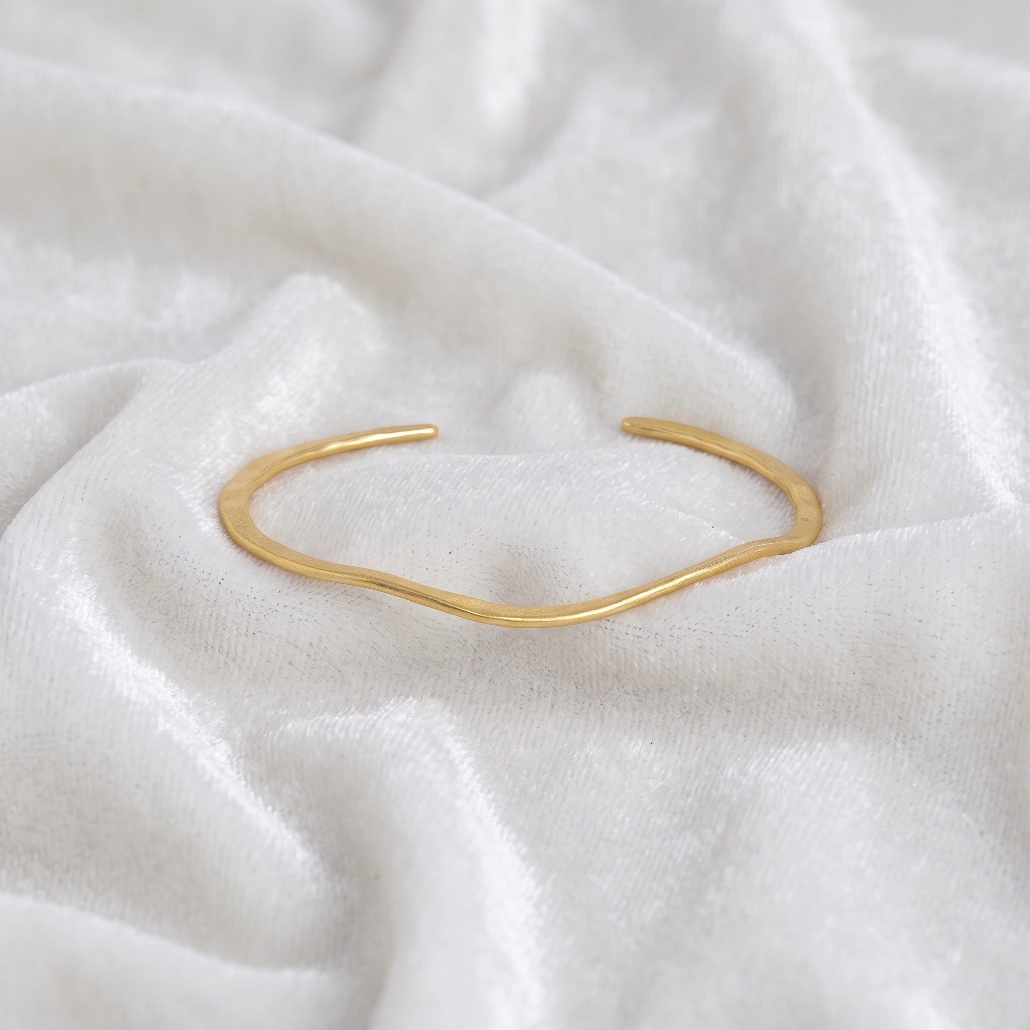 Gold_plated_bracelet_in_gold_plated_silver_with_textured_wavy_band_at_front_angle_view_on_soft_fabric_background