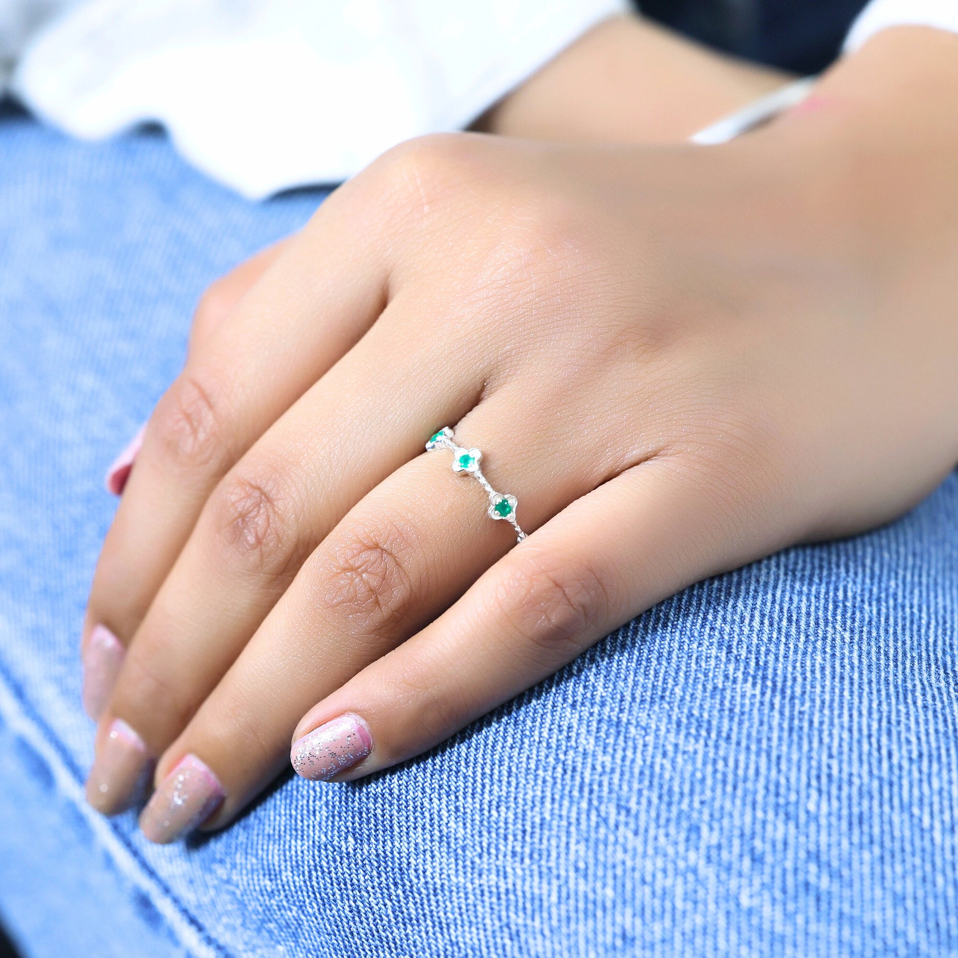 Sterling silver green onyx floral eternity band ring on a woman's hand on blue denim jeans angled straight jewelry shot.